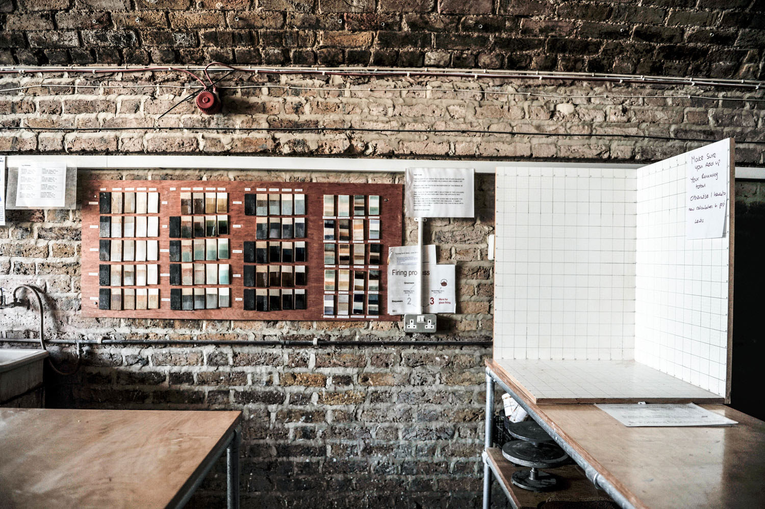 Glaze test tiles mounted on Hoxton's brick wall, beside a white-tiled glazing area and a firing process notice