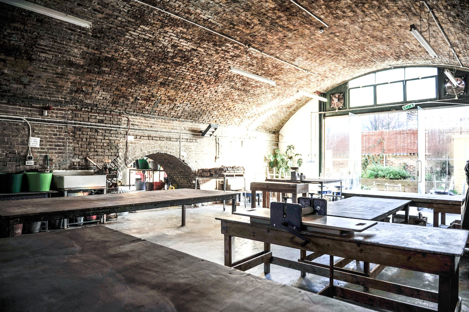 Inside the Hoxton railway arch: brick vaulted ceiling, wooden workbenches, a slab roller and glazed doors to the yard