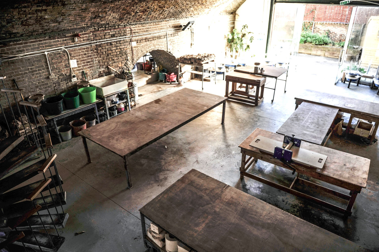 Wooden worktables, a sink and buckets under the brick arch at the Hoxton studio, with the doors open to the yard