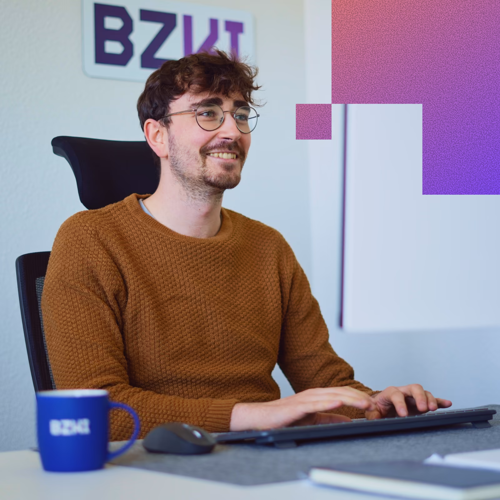 Modern office workspace with a laptop, a blue coffee mug, headphones, and a folder on a white desk, with an office chair and a person in the background.
