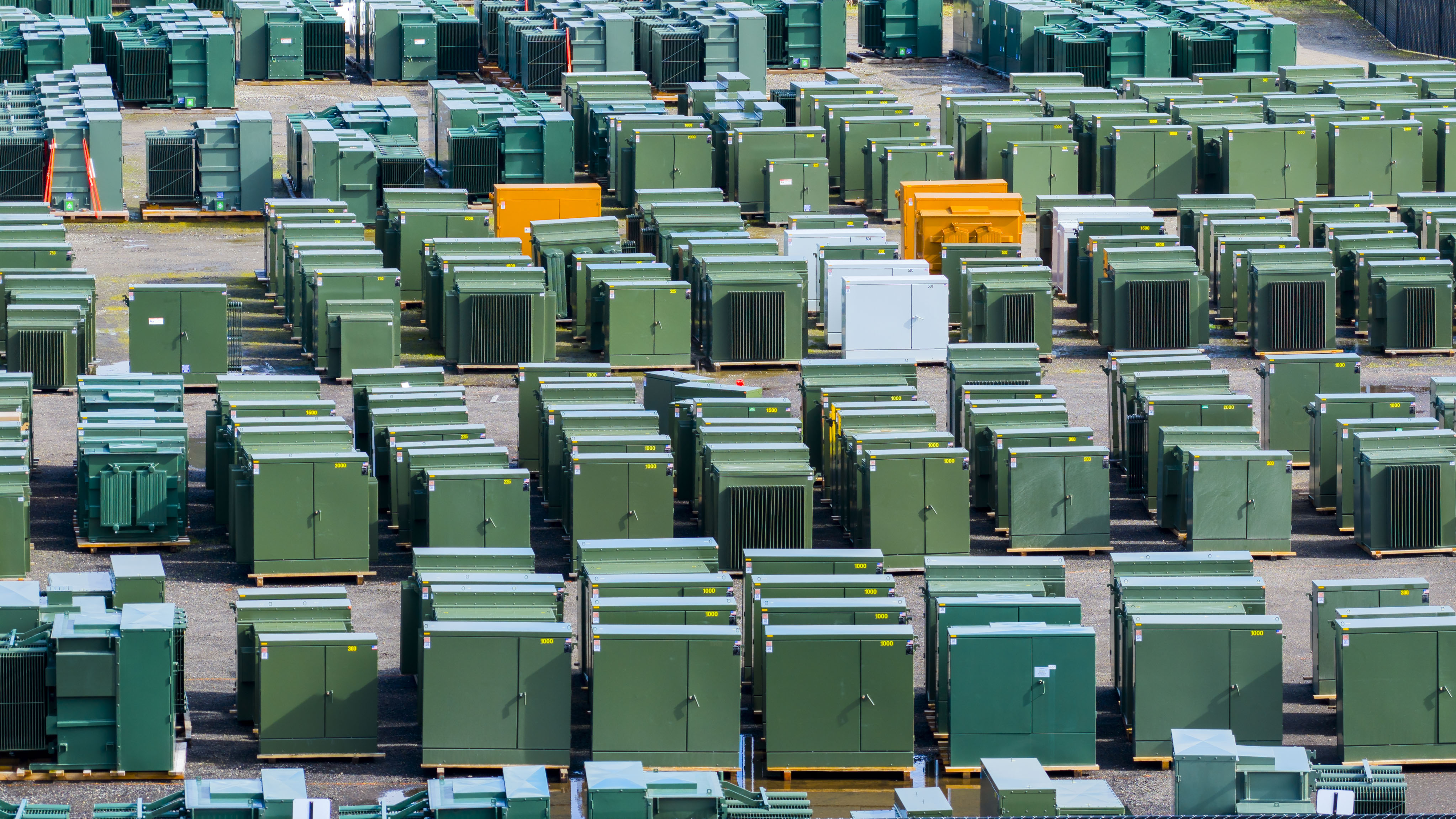 photo showing hundreds of mostly green padmount transformers in warehouse yard