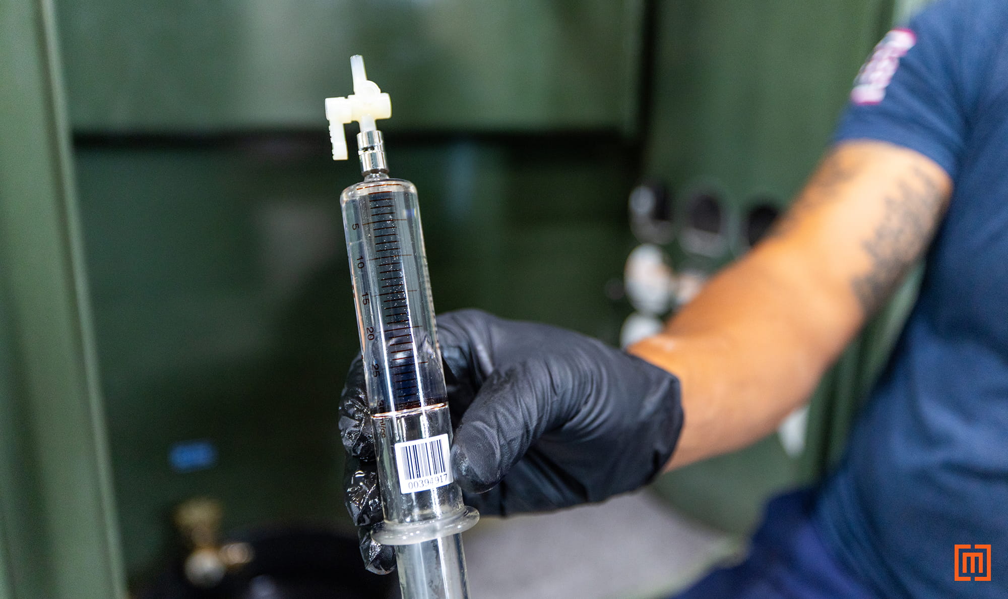 closeup of tech holding DGA sample in front of green padmount in warehousee