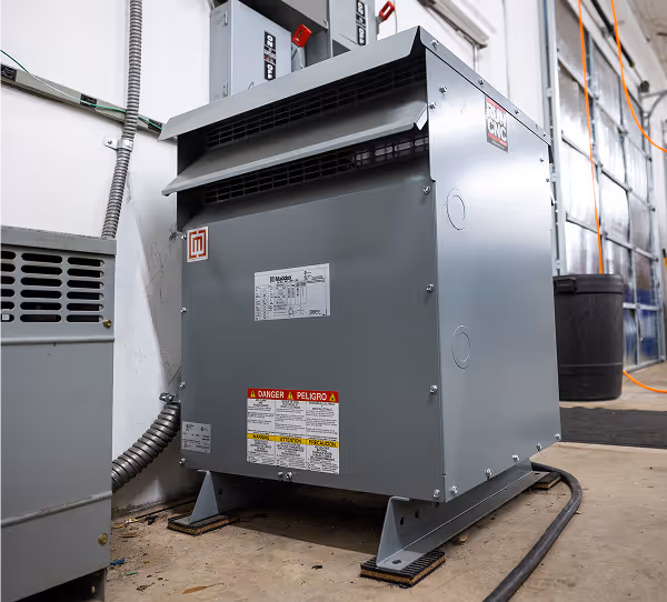 Large gray industrial electrical transformer unit mounted on a concrete floor inside a facility.