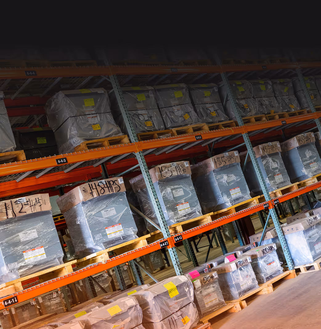 Warehouse shelves filled with large pallets wrapped in plastic and labeled with barcodes and tags.