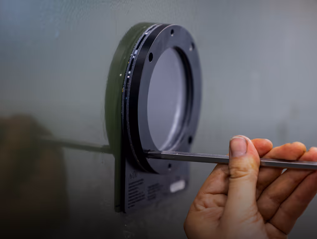 Hands using a tool to adjust or install a circular metal component on a green machine or device.