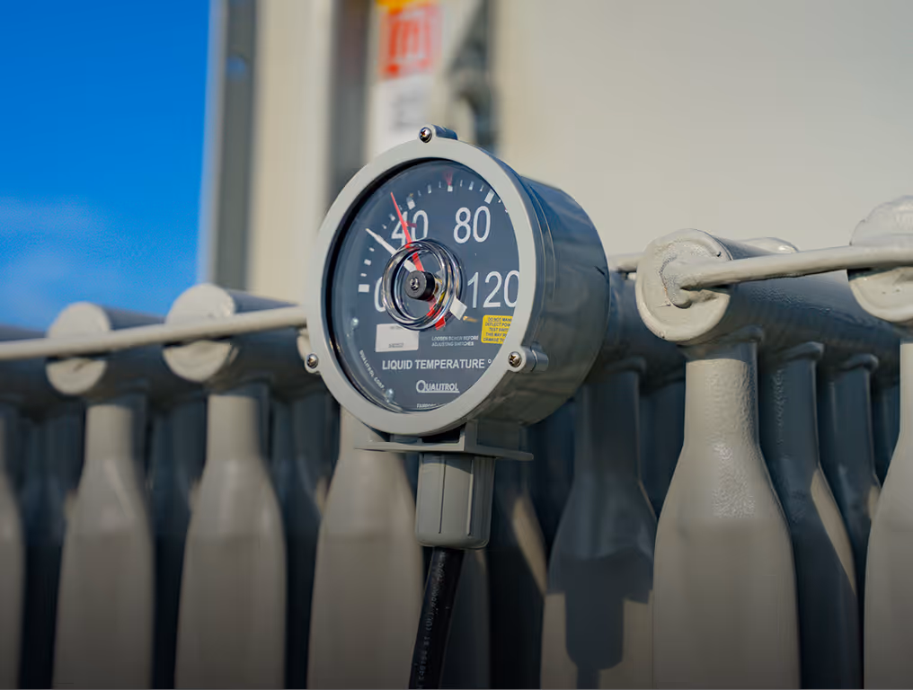 Close-up of liquid temperature gauge on gray industrial equipment with a blue sky background.