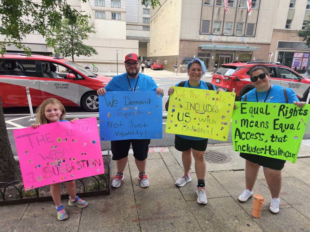 Disability Network Eastern Michigan staff and family hold signs protesting the One Big Beautiful Bill Act and demanding policy, not politics in Washington DC in July 2025.