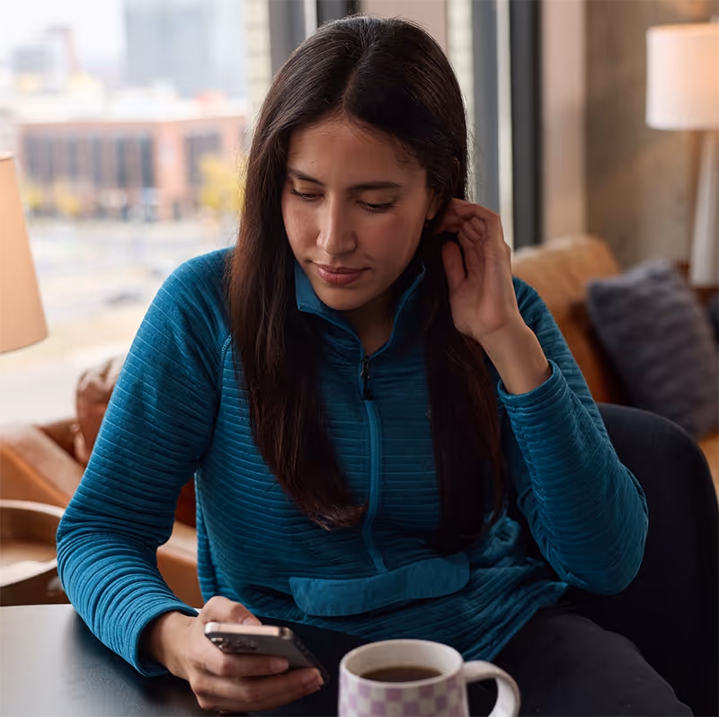Young woman looking at her smart phone while drinking coffee.