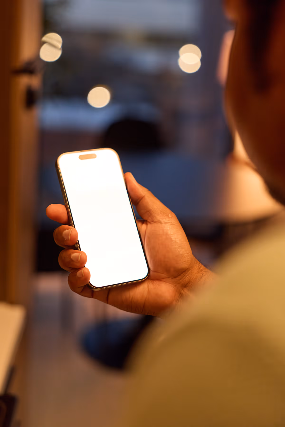 Person holding smartphone with blank white screen in a dimly lit room at night.