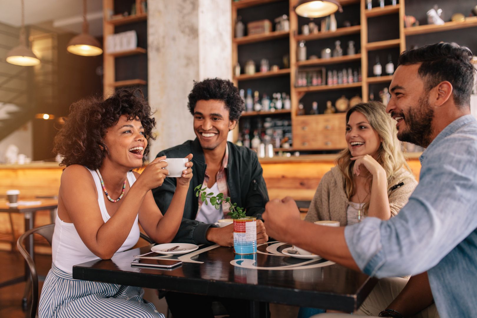 Group of four people laughing and drinking coffee together