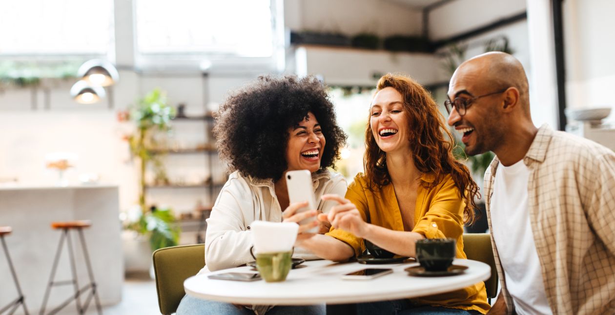 Three people smiling around a table looking at a phone