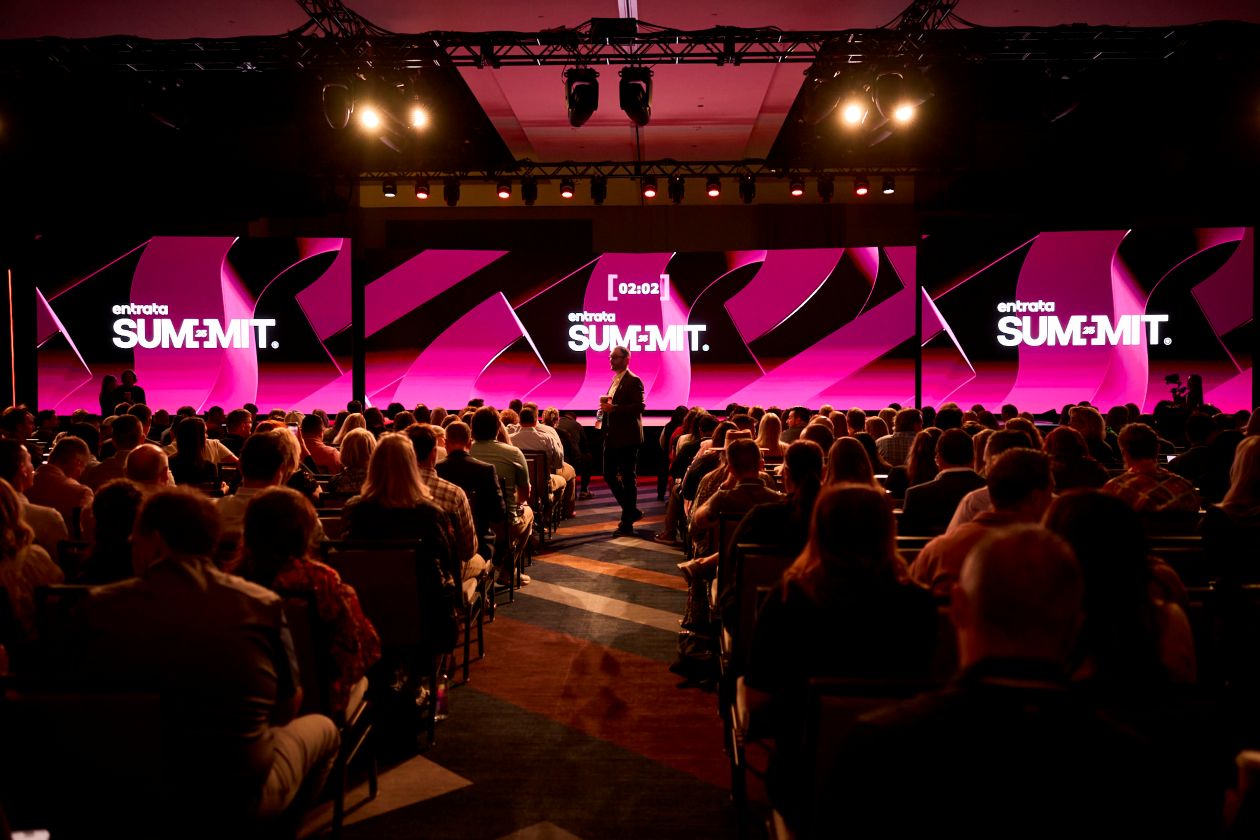 Shot of a stage that says "Summit" with a large audience sitting in front of it