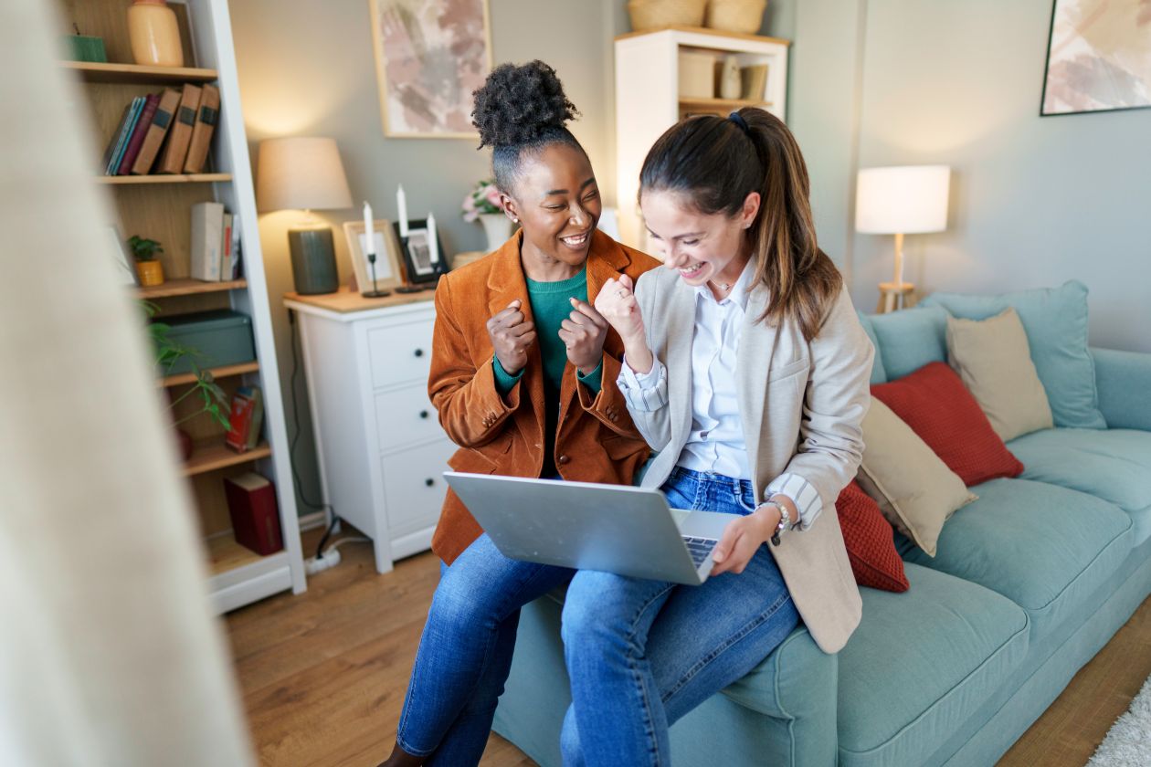 Two girls sitting on a couch smiling at a computer