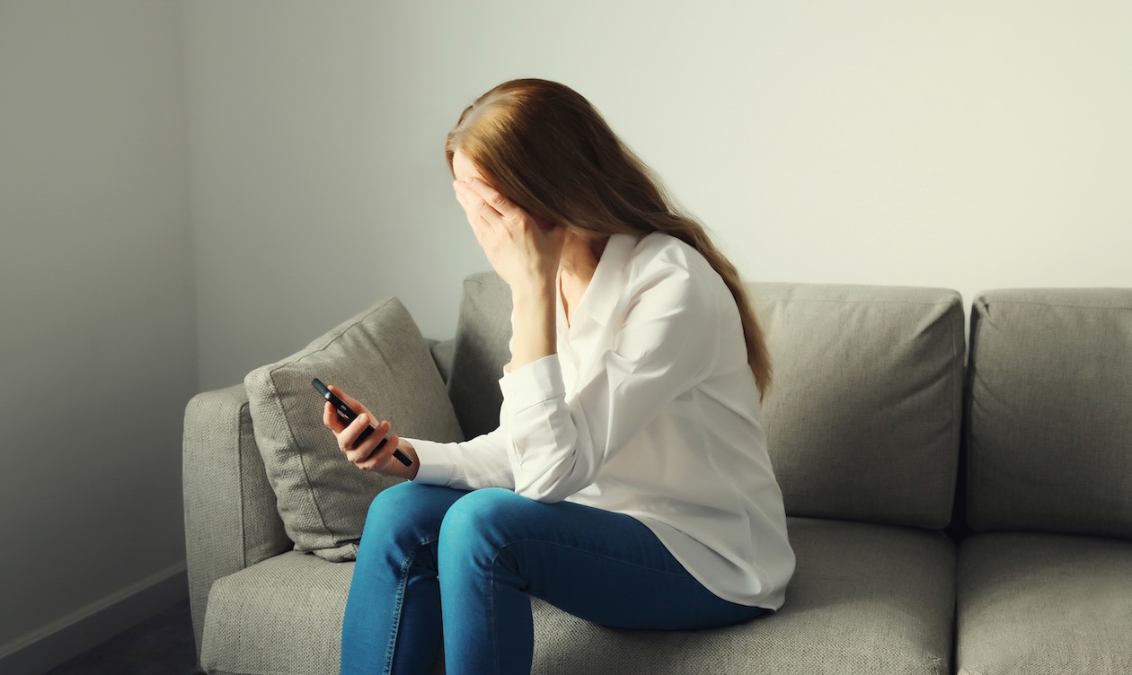 A person sitting on a couch looking at their phone is dismay