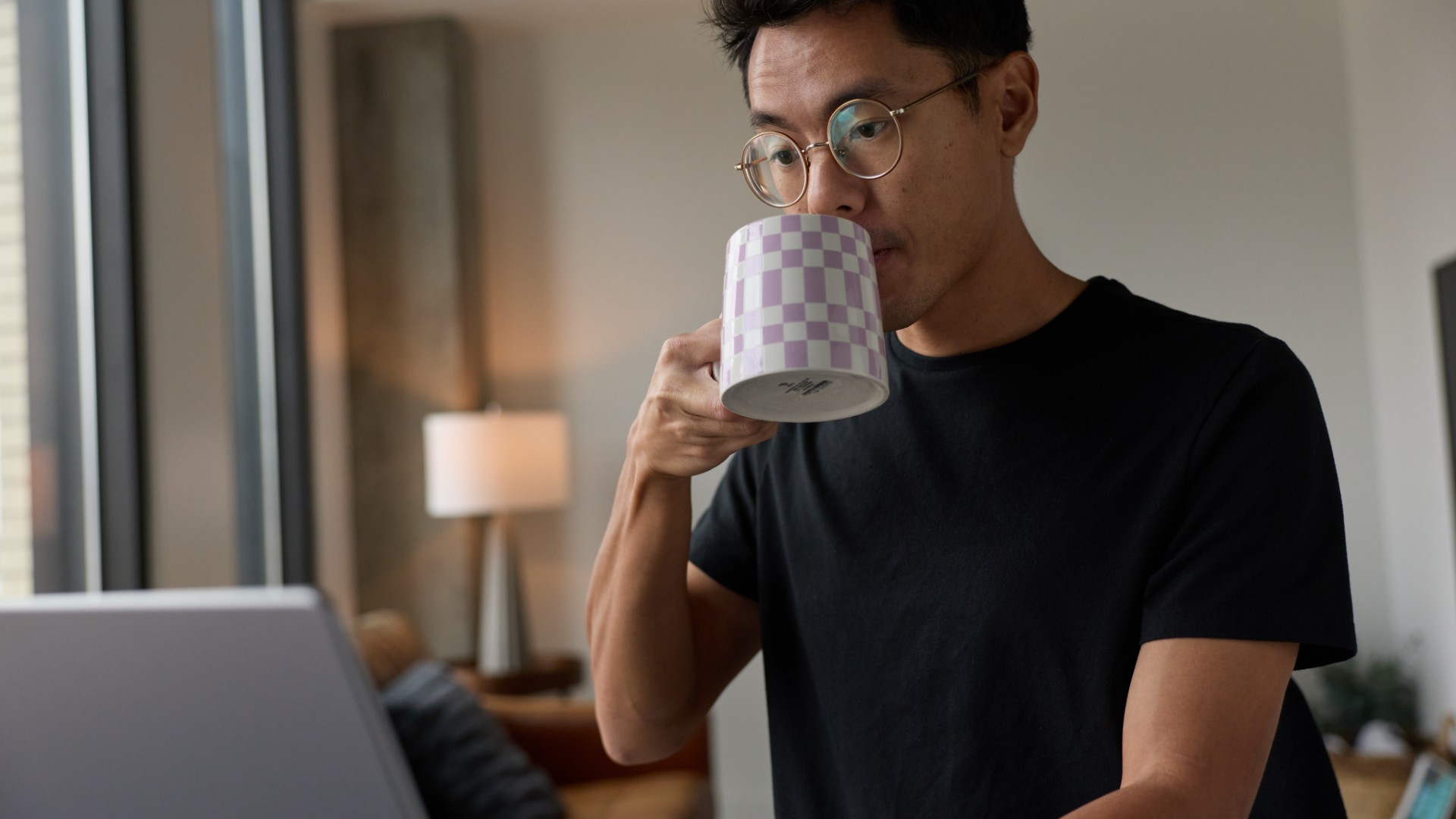 A person sitting a table looking at their laptop while sipping a cup of liquid