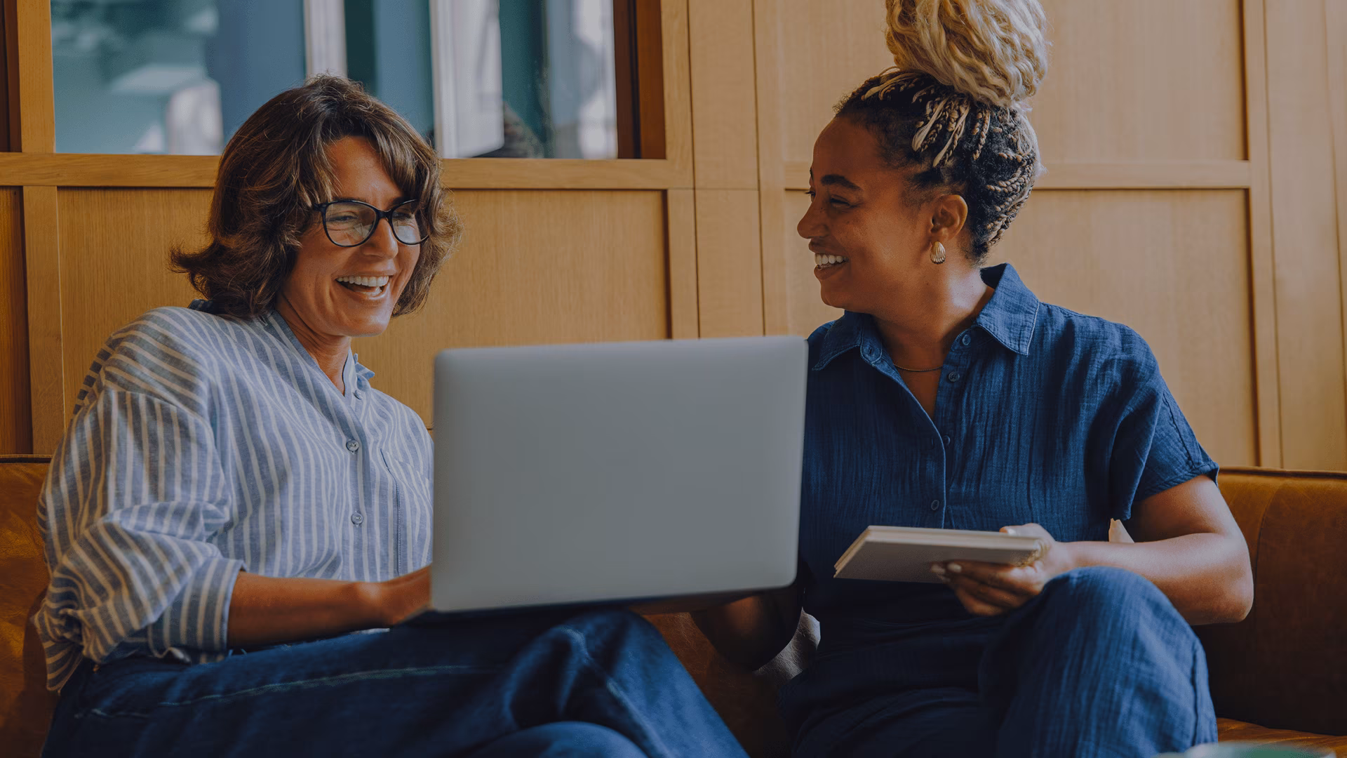 Two women sitting on a couch discussing business with an open laptop