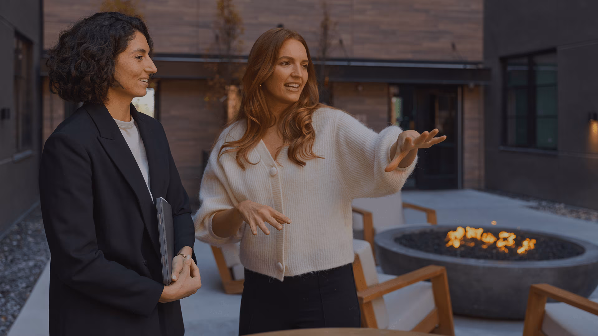 Women speaking outside of an apartment building, one has her arm raised to the side