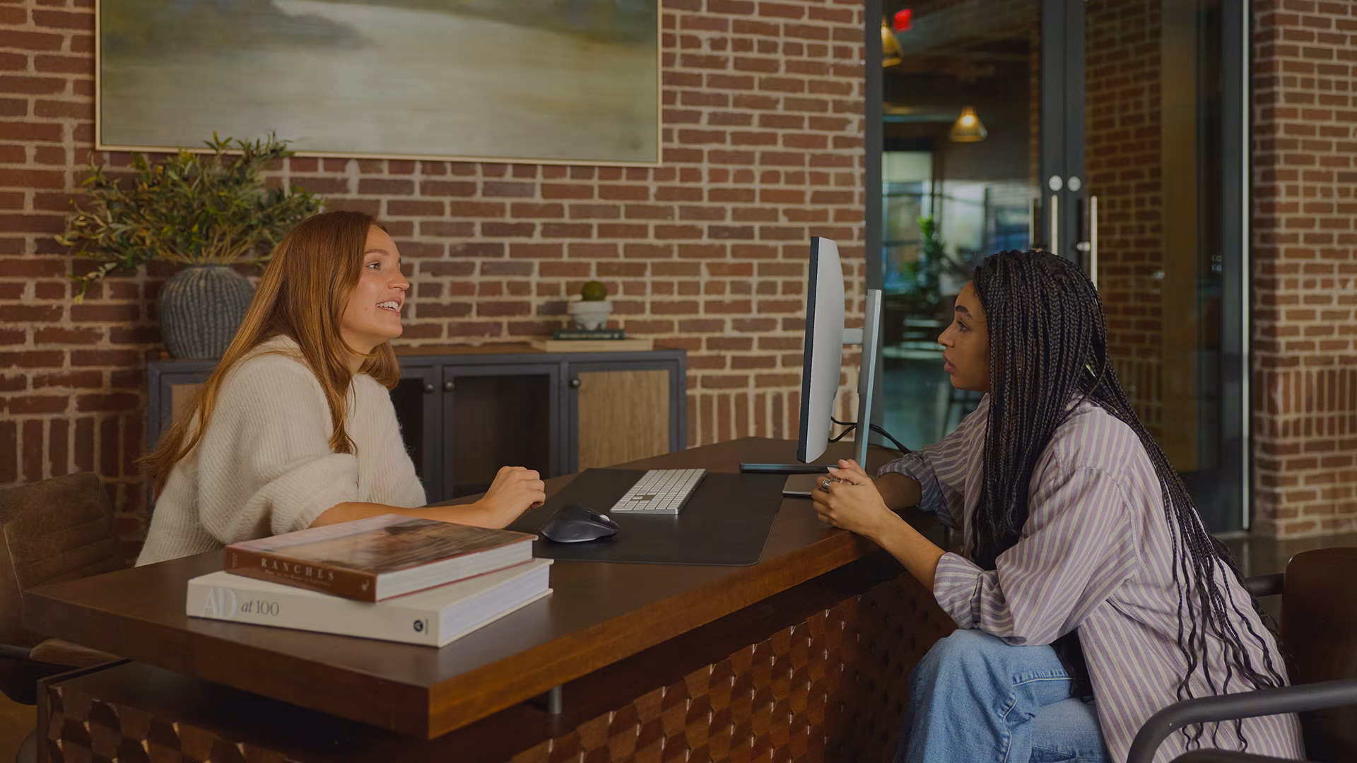 Two women sitting at a desk with a computer and having a conversation