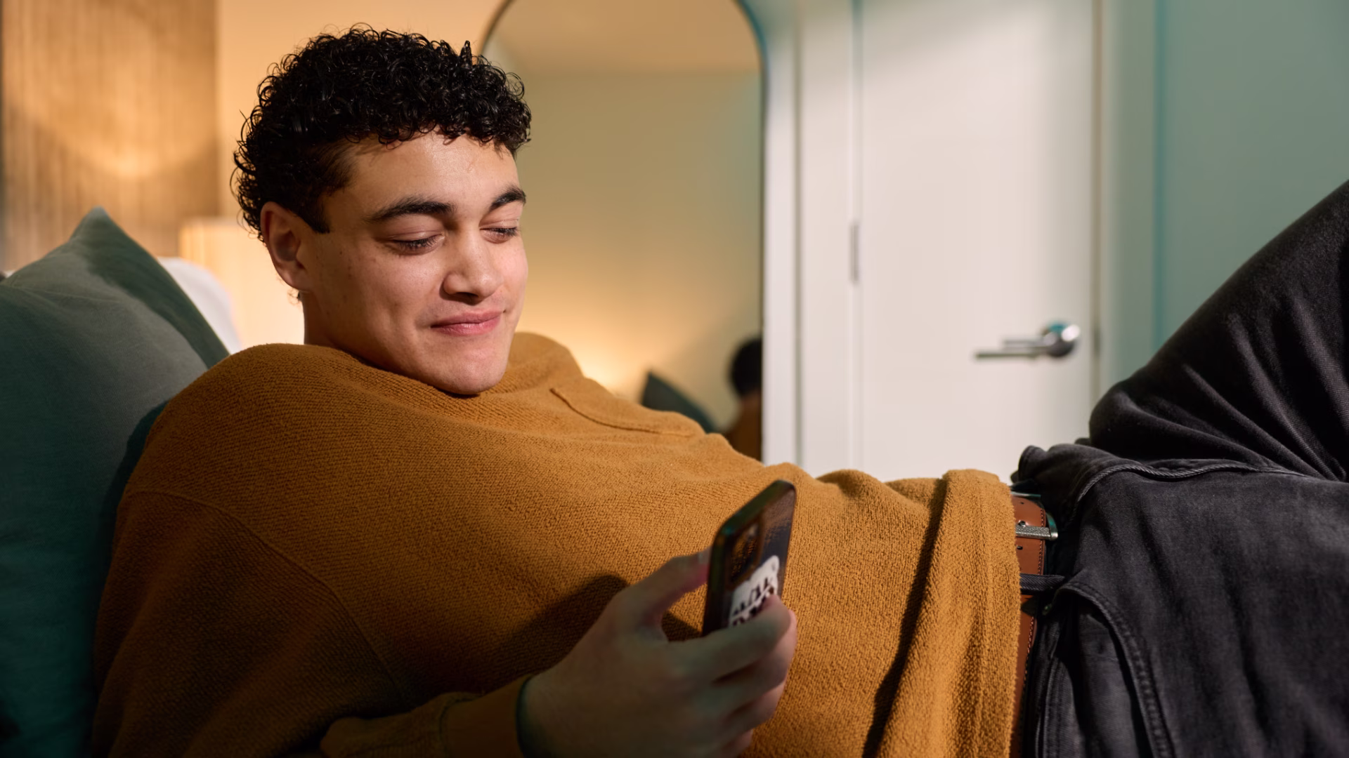 A person laying on a couch looking at their smartphone smiling