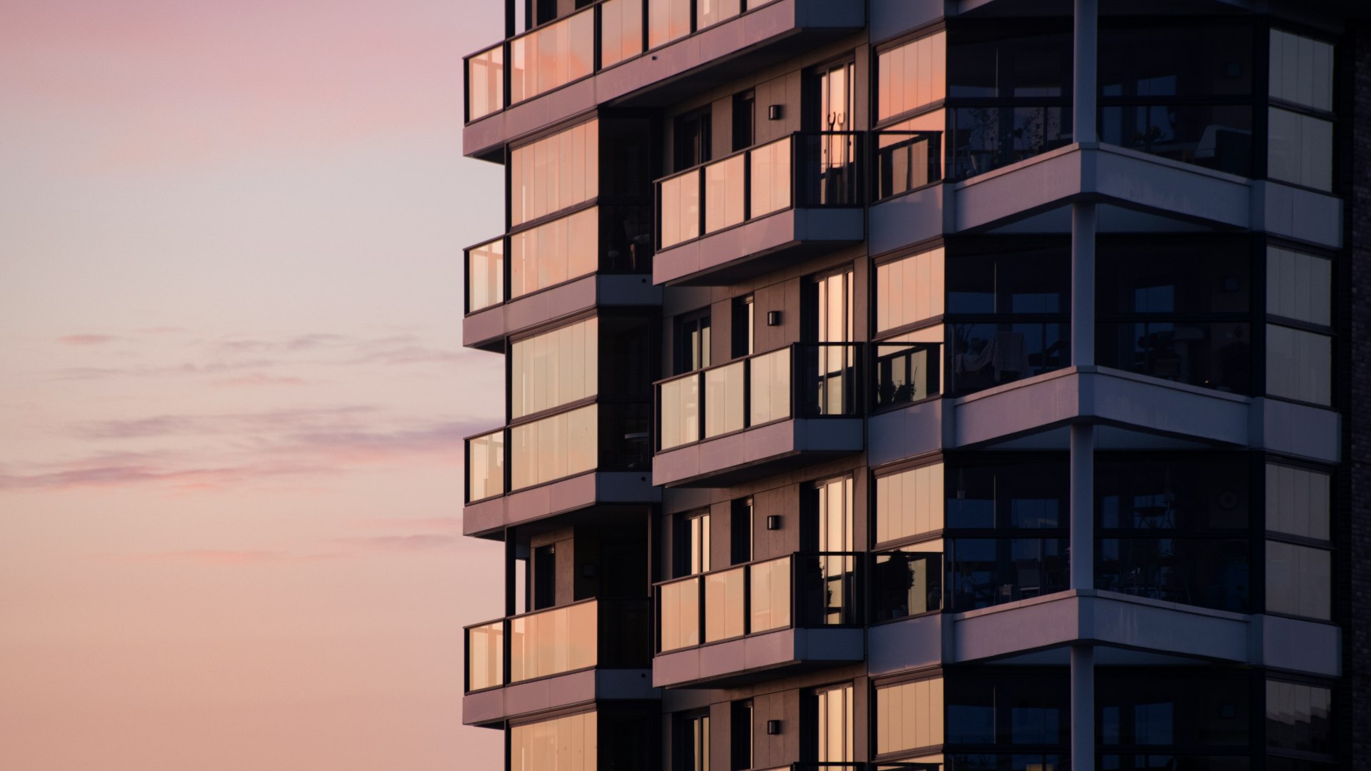Modern apartment building with glass balconies at sunset.