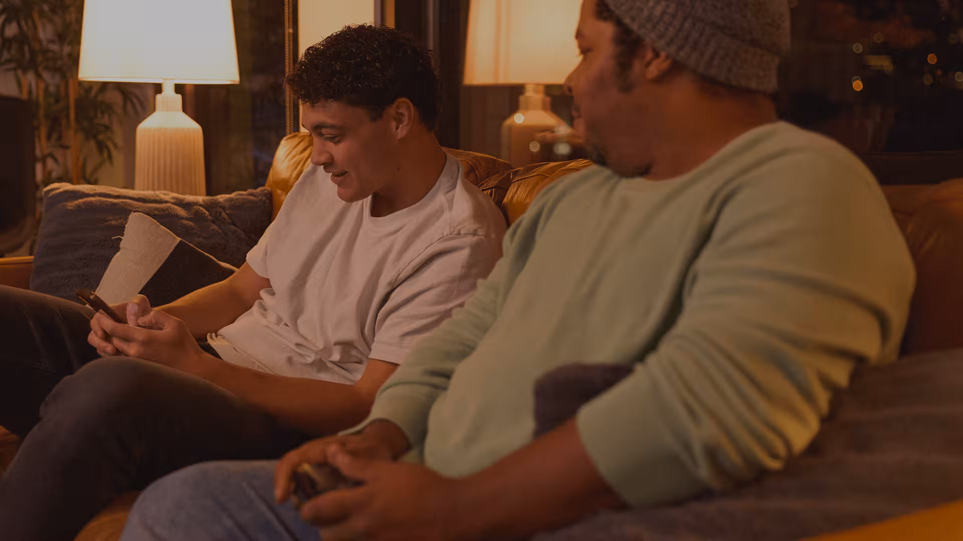 Two men sitting on the couch looking at a cell phone