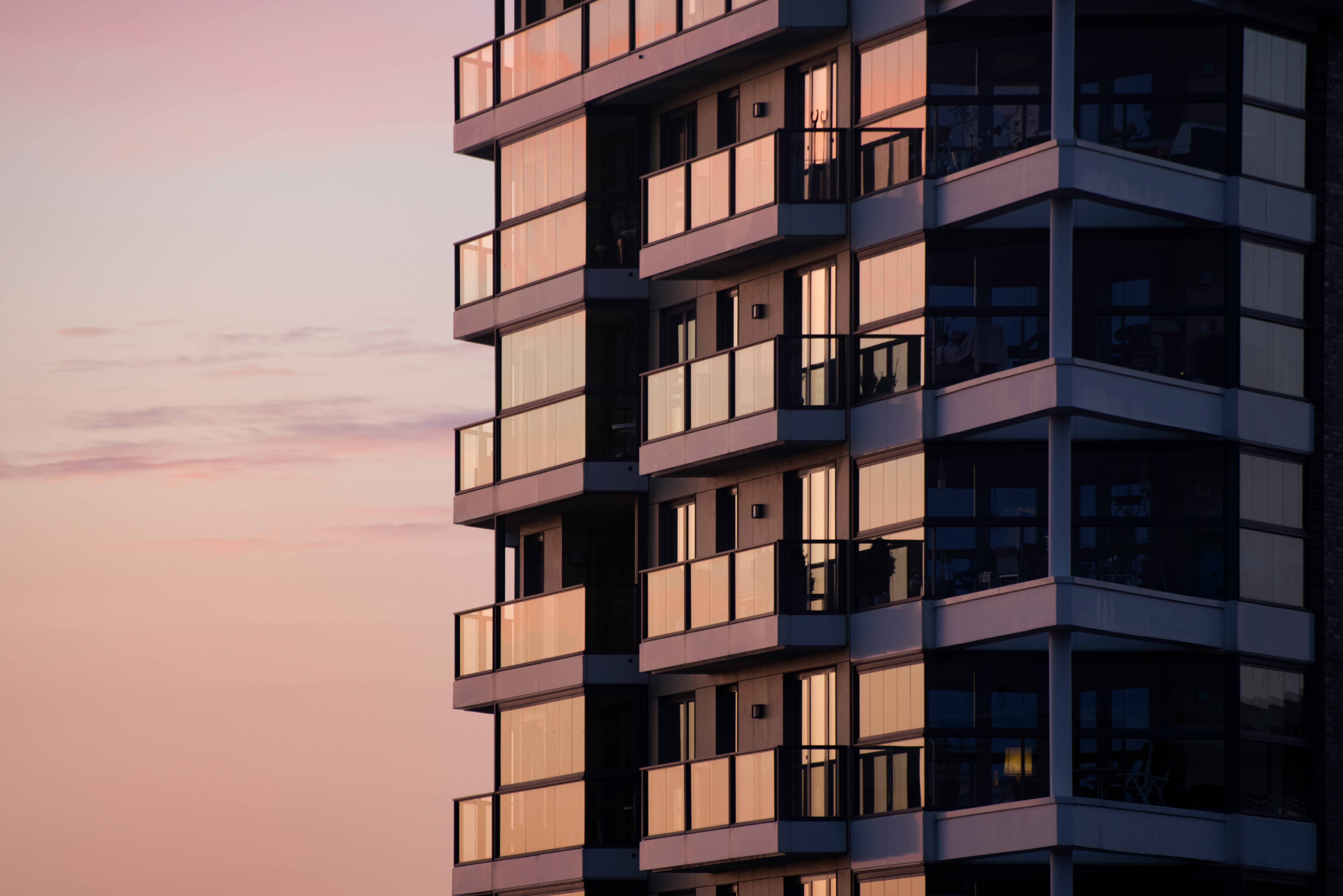 A neutral colored high rise apartment building with a sunset lit sky in the background