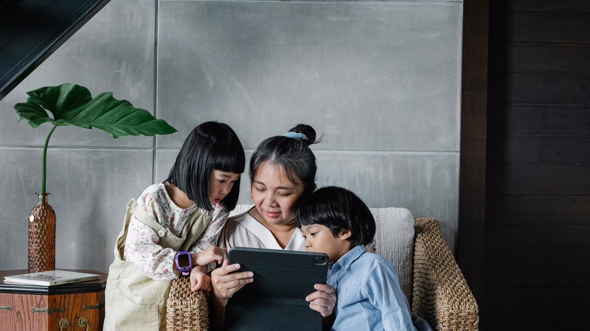 a mother and her two children sitting on a ouch looking at a tablet