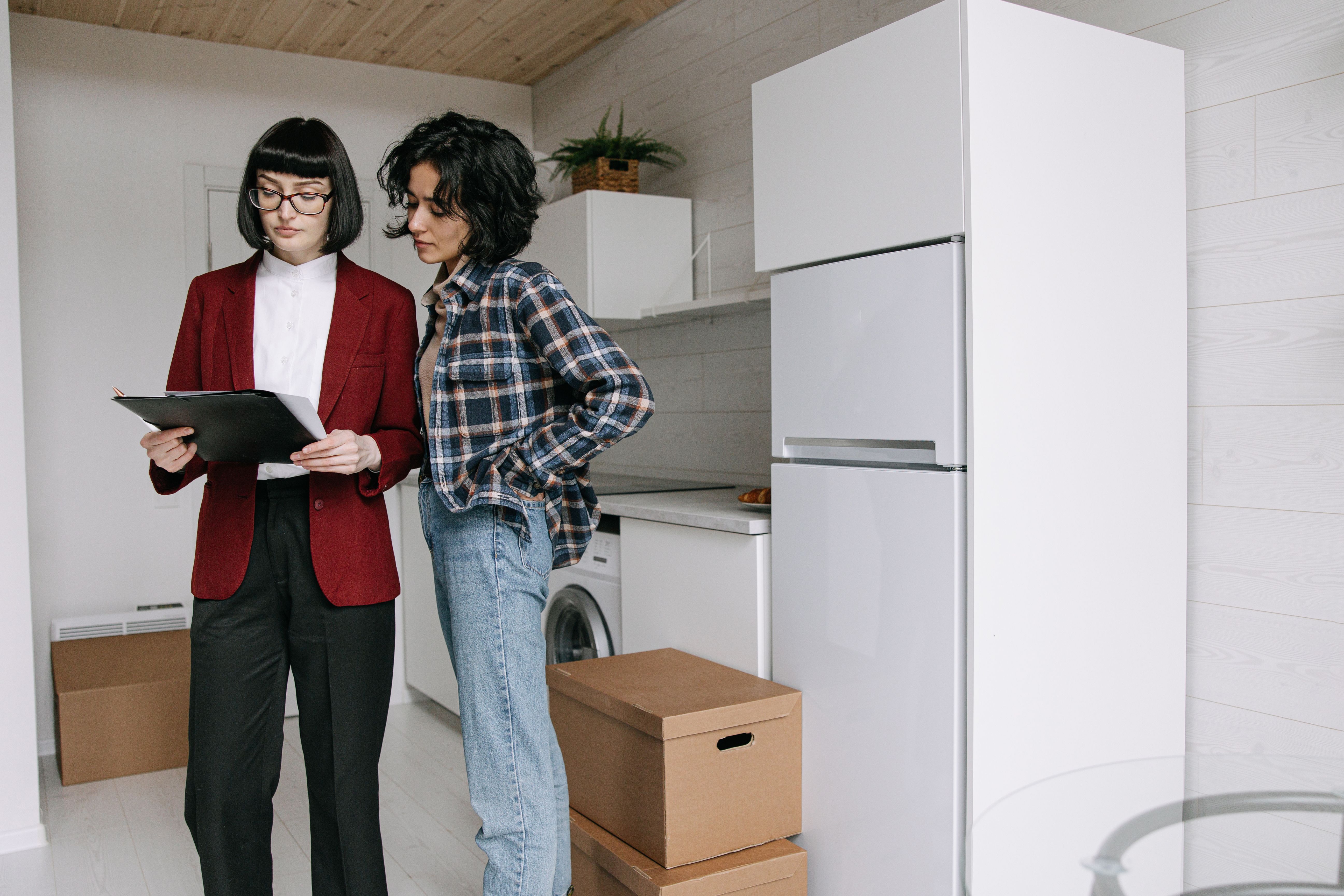 A property manager reviewing a checklist on a clipboard with a tenant in a kitchen.