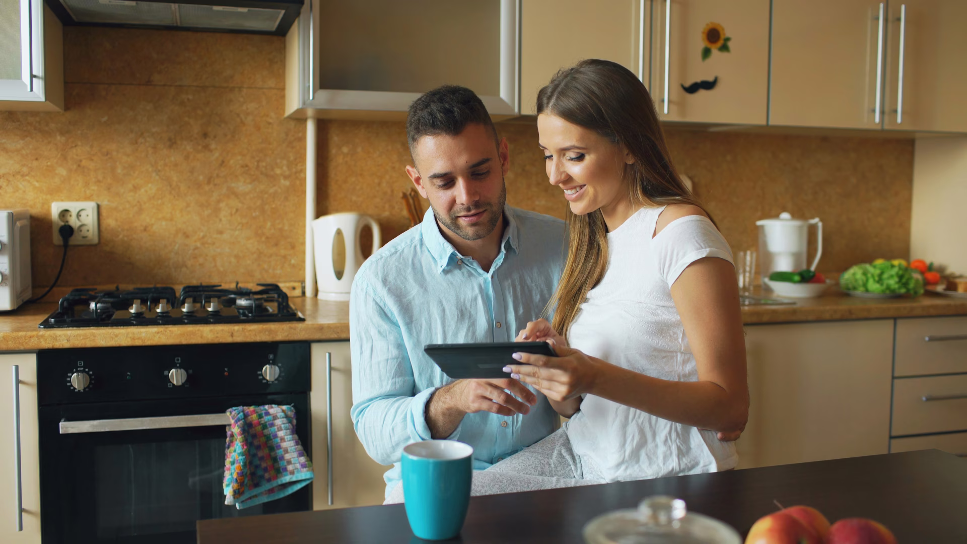 a man and a woman in a kitchen looking at a tablet