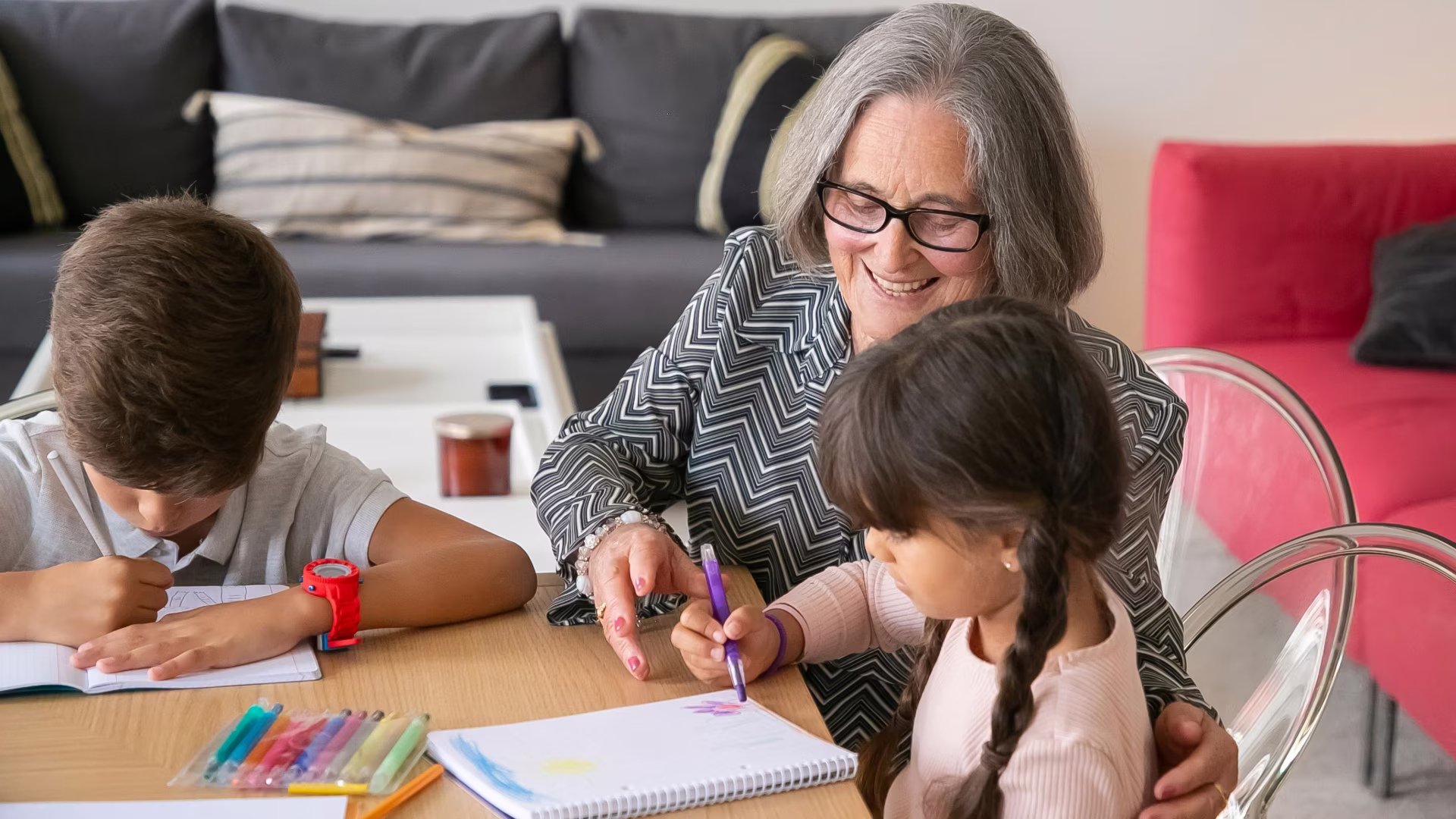An older person smiling and laughing with two children sitting at a coffee table