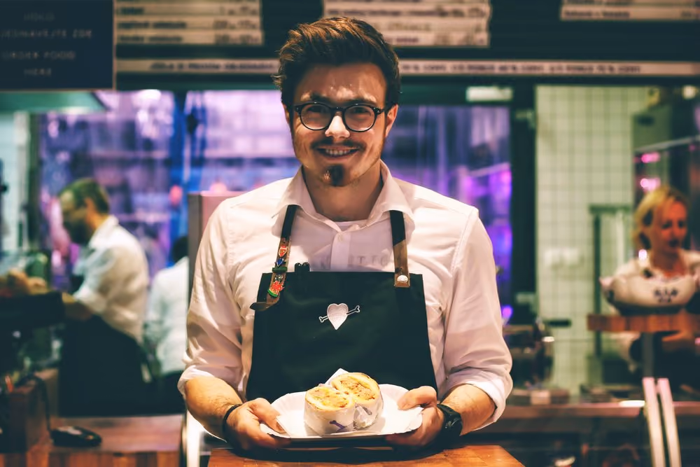 A man in an apron proudly presents a plate of delicious food, showcasing his culinary skills and passion for cooking. 