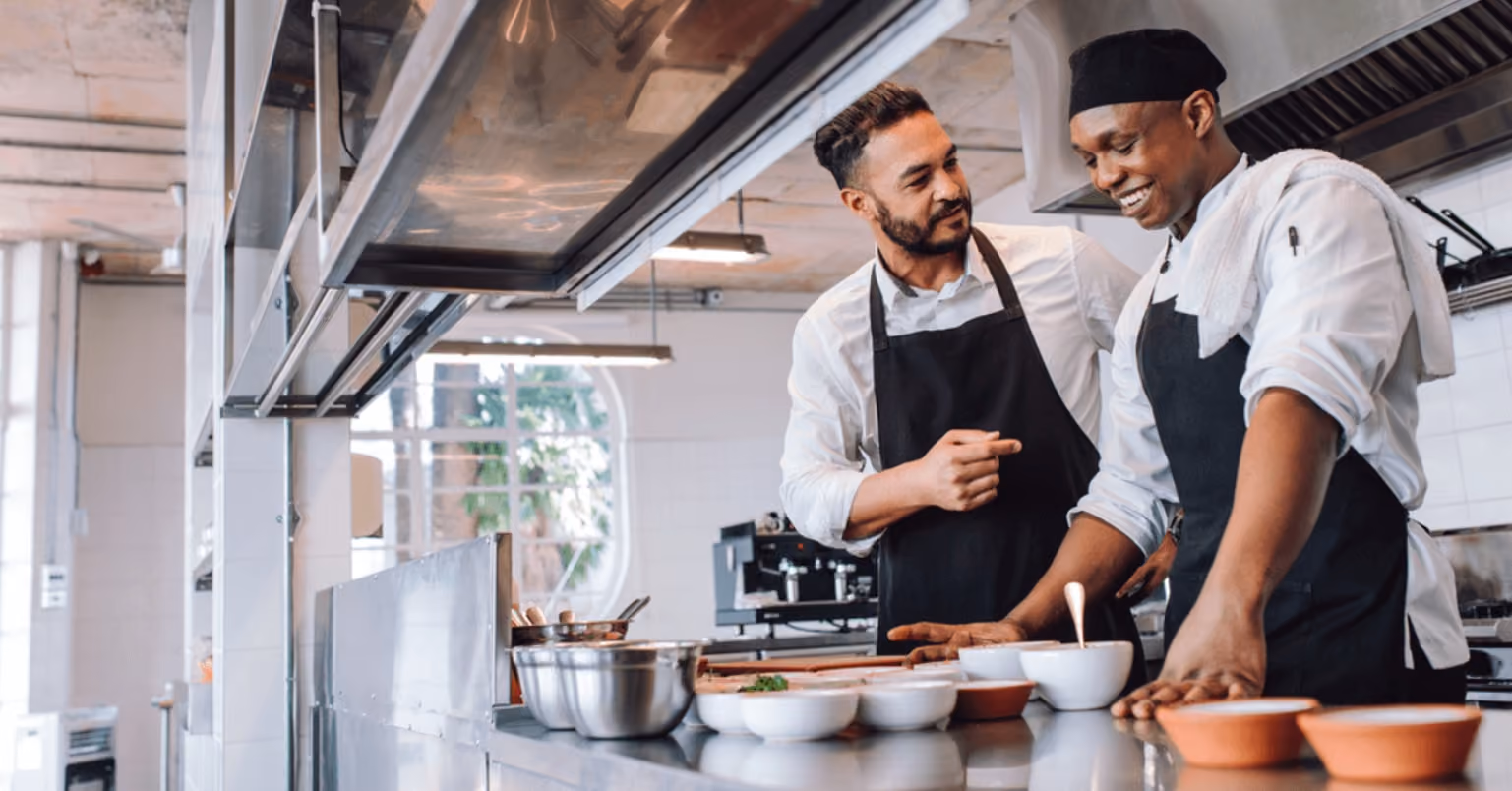 Two chefs collaborating in a bustling commercial kitchen, focused on preparing a delicious meal.