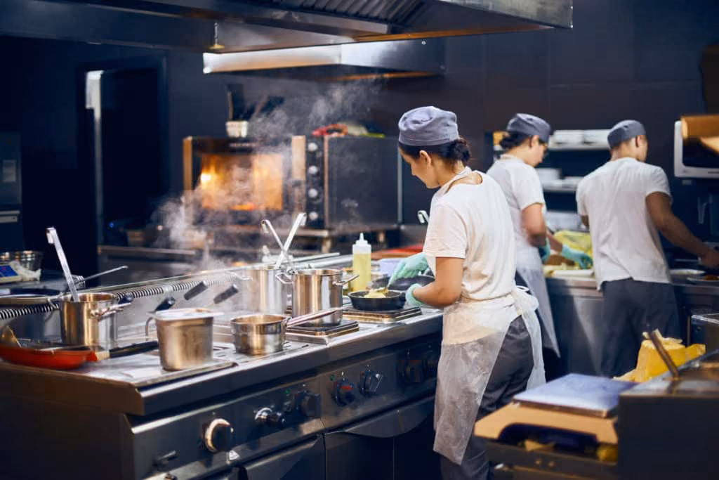 A woman preparing food in a kitchen with two men behind her working