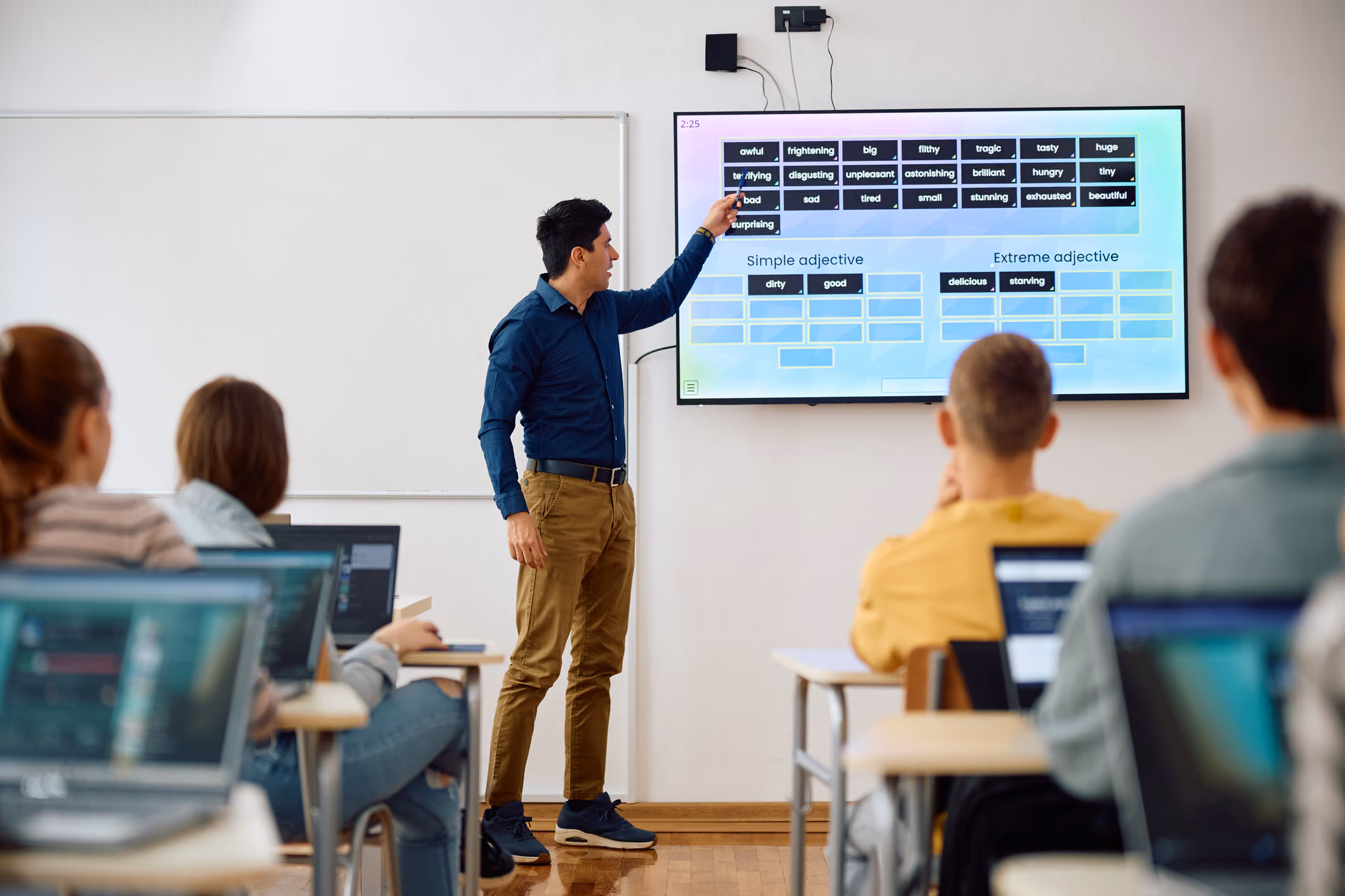 A man teaching a classroom full of children using a digital screen