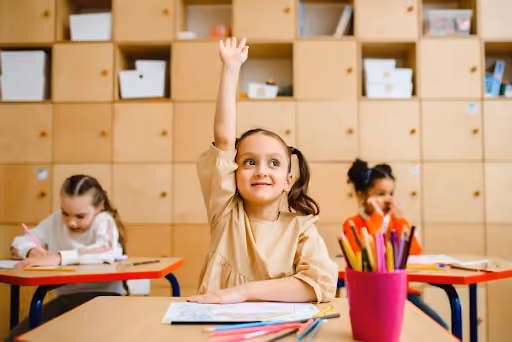 A little girl in a classroom with her hand raised