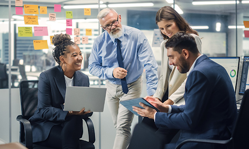 Four individuals seated at a table, each using a laptop, engaged in a collaborative work session.