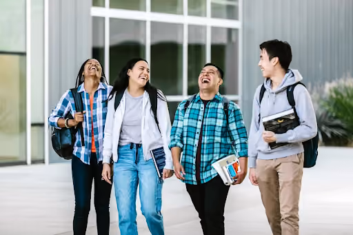 4 people walking on campus holding books and laughing