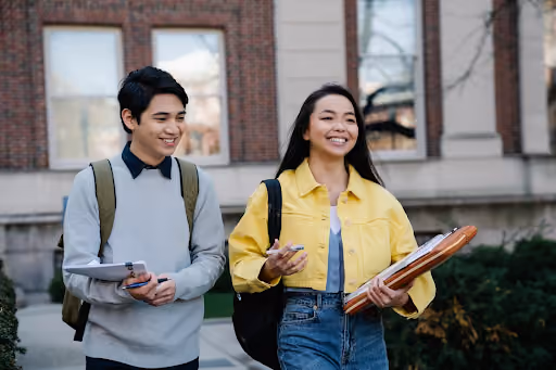 Two people walking on campus holding books engaging in conversation