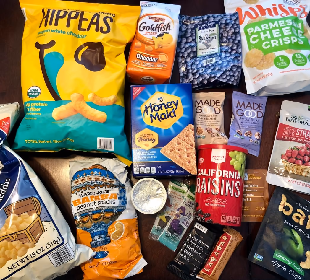 A variety of snacks, including chips, fruits, and candies, are arranged neatly on a table for a gathering.
