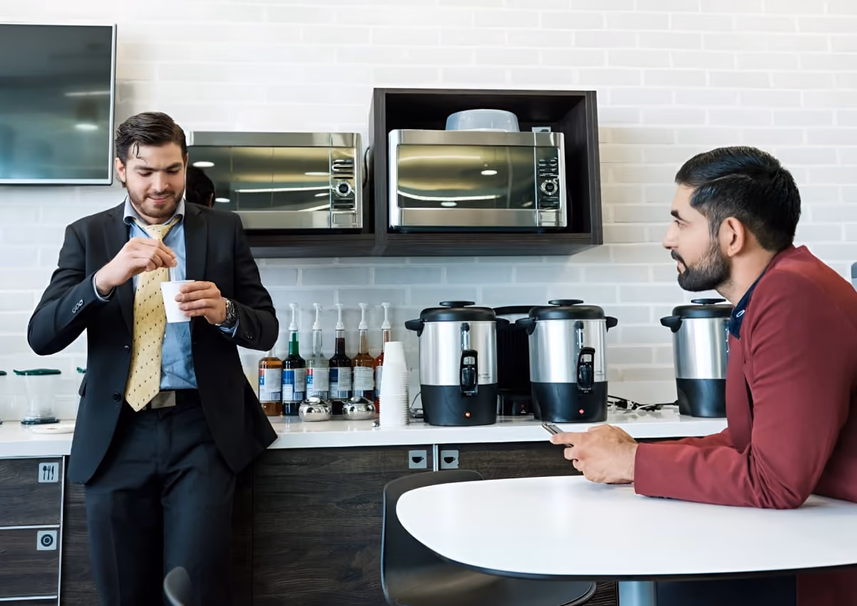 Two men in suits standing in a modern kitchen, discussing plans with a professional demeanor.
