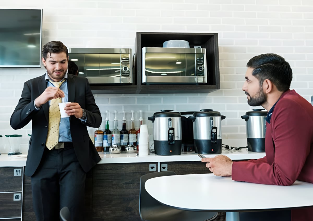 Two men in suits standing in a modern kitchen, discussing plans with a professional demeanor. 