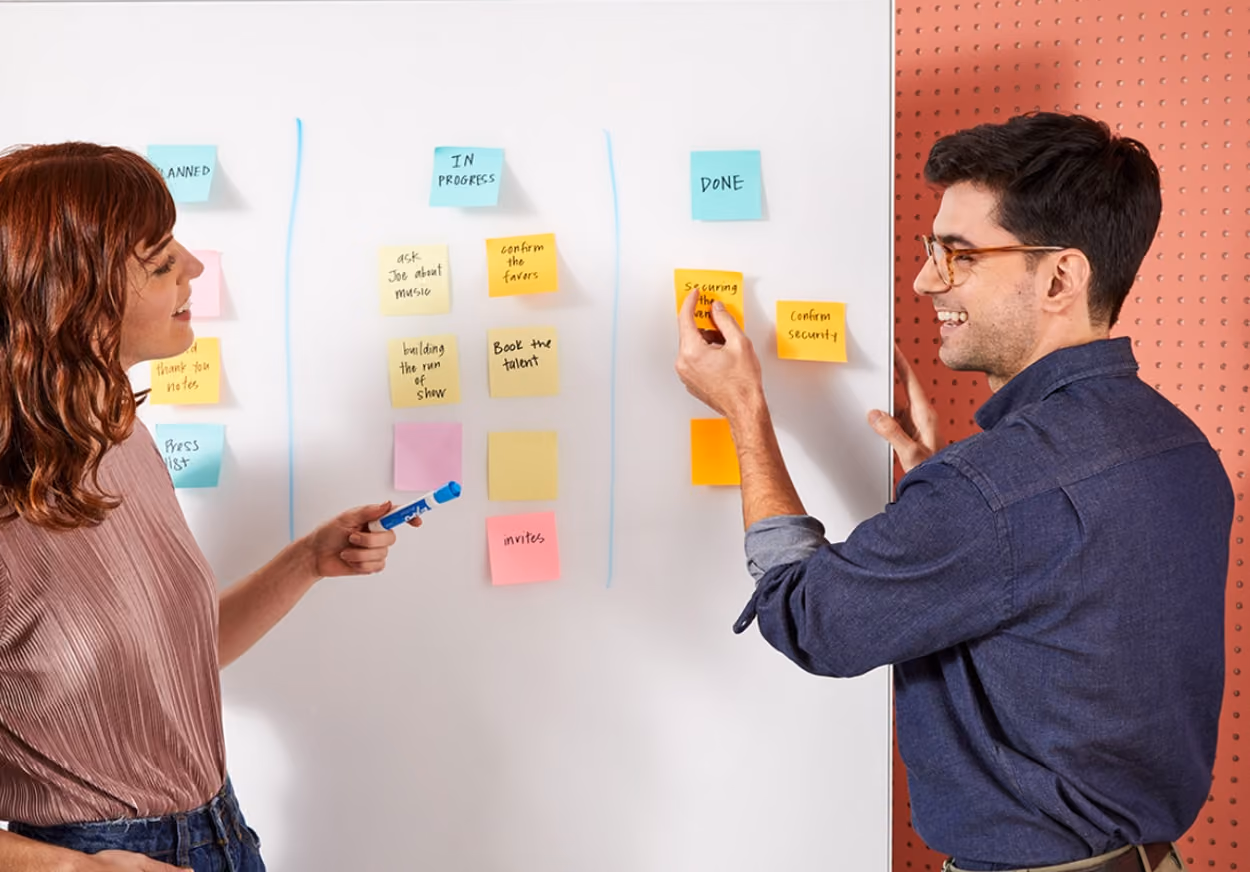 A man and woman stand beside a whiteboard covered in colorful sticky notes, discussing ideas collaboratively.