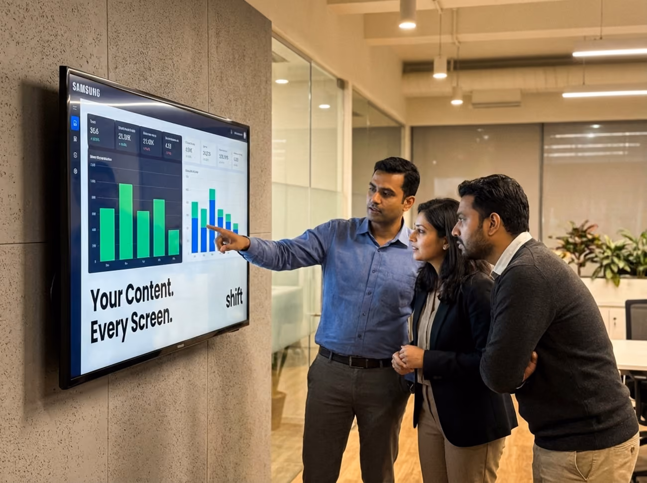 Three individuals observe a large screen displaying various graphs and data visualizations in a professional setting.