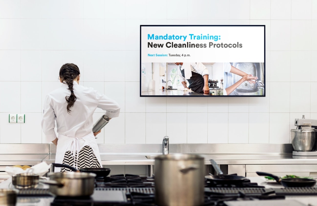 A woman stands in front of a television displaying a menu, looking engaged and ready to select an option.  