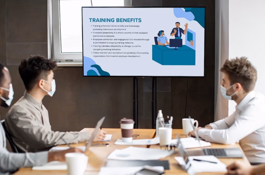 A group of people in a meeting room watching a presentation displayed on a screen.