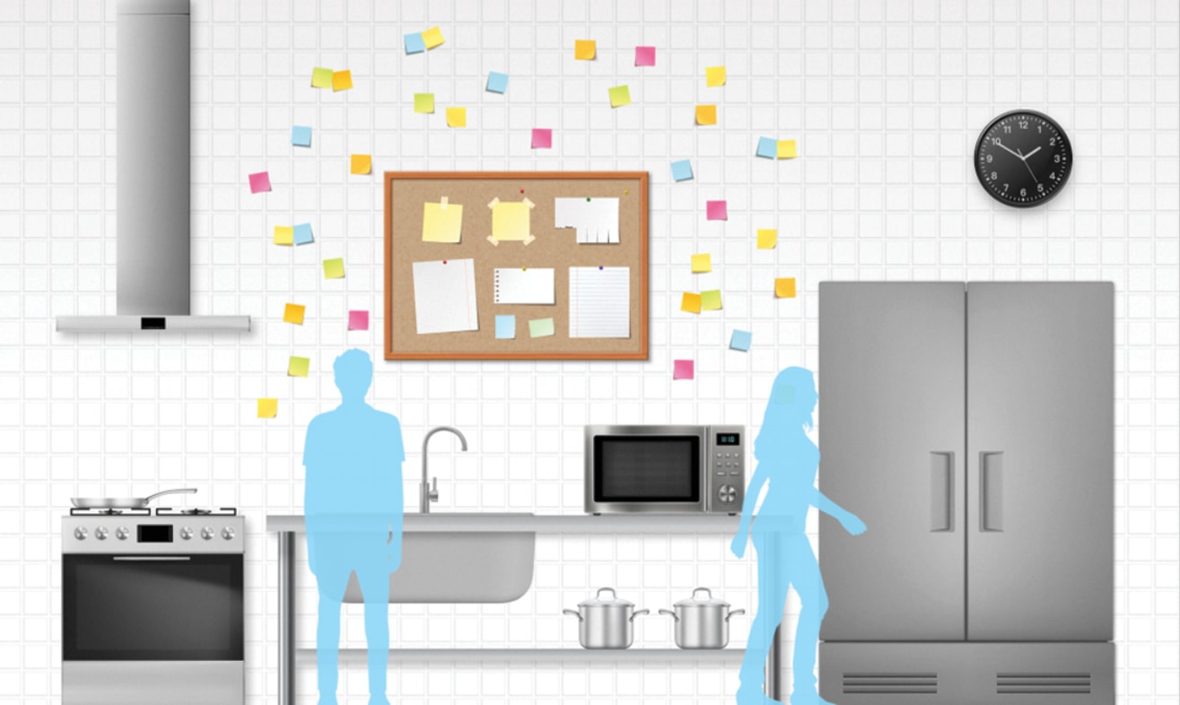 A couple poses in front of a kitchen equipped with a refrigerator, microwave, stove, and sink.