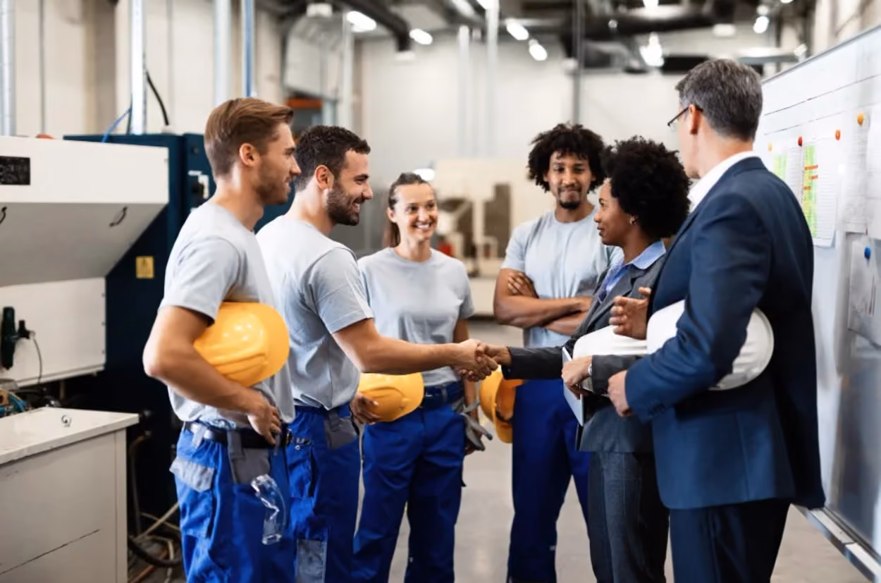 A group of factory workers shaking hands, symbolizing teamwork and collaboration in a manufacturing environment.