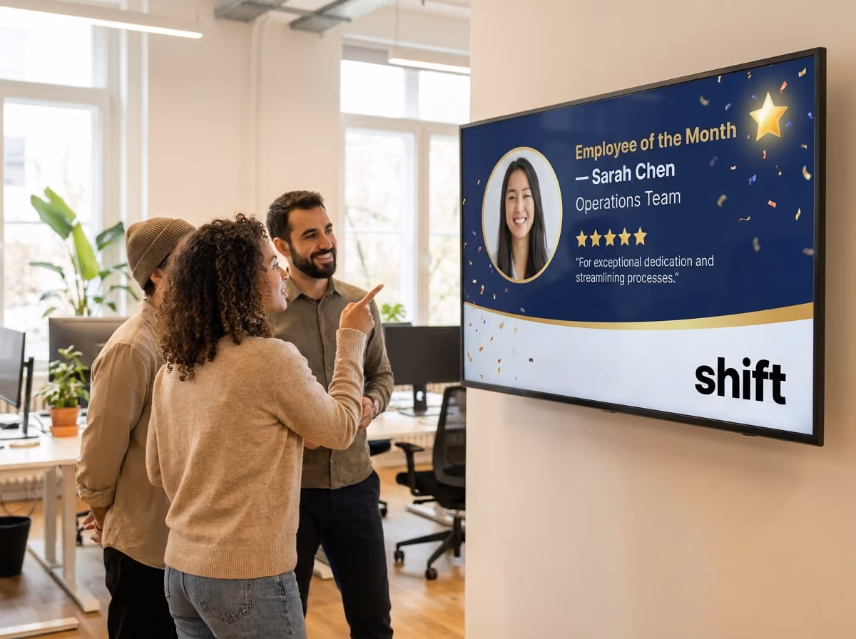 Three colleagues admire an "Employee of the Month" display featuring Sarah Chen from the Operations Team in a modern office.