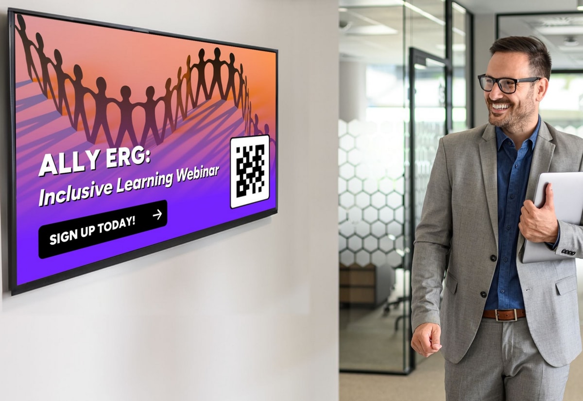 Man in a suit smiles at a wall screen showing "ALLY ERG: Inclusive Learning Webinar" with a QR code and "SIGN UP TODAY!" button, in a modern office.