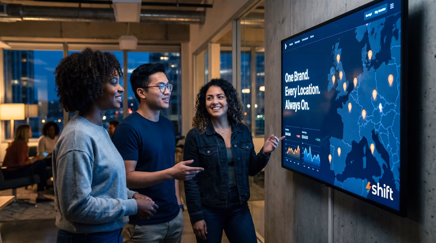 Three people discuss a digital map display in an office, highlighting global locations with the slogan "One Brand. Every Location.